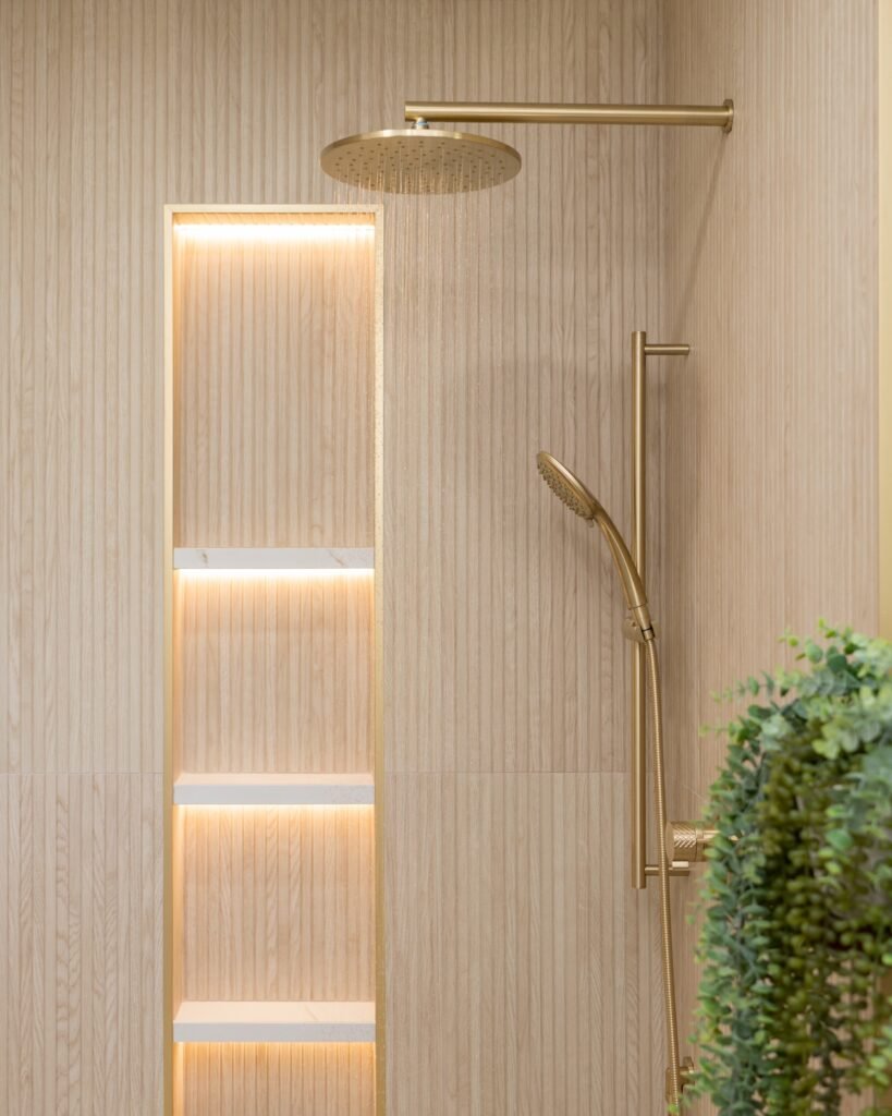 Brushed brass rain shower running beside a three-shelf backlit niche