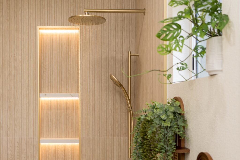 Brass rain head and handheld slide bar next to the lit niche in the remodeled shower