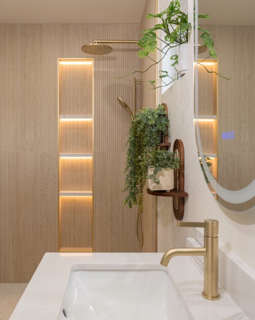 Marble-look vanity top and brushed brass tap with the lit shower niche reflected in the mirror