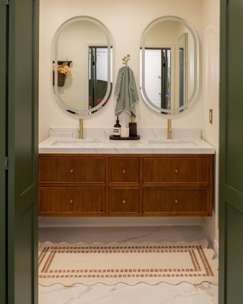 Double vanity in fluted walnut under two oval backlit mirrors