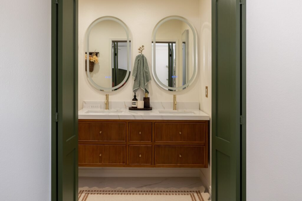 Double vanity and backlit oval mirrors seen through the green bathroom doors